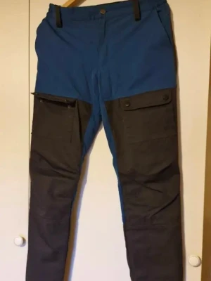 Blå och svart fritidsbyxa - Snygg byxa i blått och svart med raka ben och fickor. Byxorna har bälteshällor och är tillverkade i ett slitstarkt material, perfekt för naturen o friluftsliv str C170, är som en Medium