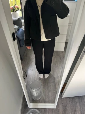Svart jacka från Nelly  - Säljer en svart jacka från Nelly med framfickor och knäppning framtill. Jackan har klassisk krage, långa ärmar med muddar och en rak, något boxig passform. Perfekt för dig som gillar stilrena och enkla plagg.
