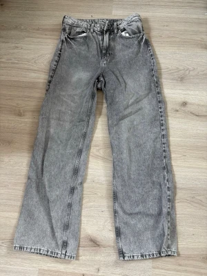 Grå raka jeans med vintagekänsla - Säljer ett par grå jeans med rak passform och klassisk femficksdesign. Jeansen har en tvättad look som ger en schysst vintagekänsla och passar perfekt till en avslappnad stil. Materialet är denim i bomull och de har bälteshällor och knappgylf.