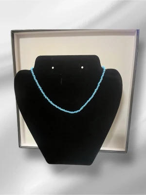 Blått pärlhalsband med guldlås - Ett stilrent halsband med små, runda blå pärlor och ett snyggt guldfärgat lås. Perfekt för att ge din outfit en färgklick. Halsbandet har en enkel och modern design som passar till många olika stilar.halsbandet är handgjord