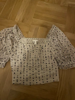 Prickig blus från H&M - Supersöt blus från H&M i ljus färg med svarta prickar. Tillverkad i ett tunt, transparent material som ger en luftig känsla. Perfekt för dig som gillar trendig stil.