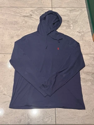 Mörkblå hoodie från Polo Ralph Lauren - Snygg mörkblå hoodie från Polo Ralph Lauren med klassisk huva och dragsko. Liten röd logga broderad på bröstet. Hoddien är väldigt tunn men passar till allt.