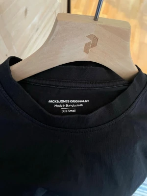 Svart t-shirt från Jack & Jones - En stilren svart t-shirt från Jack & Jones Originals med tryck 'Originals Studio' på bröstet. Klassisk rund halsringning och korta ärmar. Tillverkad i mjuk bomull som känns skön mot huden. Perfekt för en clean och enkel look.  OBS! Tröjans färg är i verkligheten som på första bilden. Den är väldigt sparsamt använd då den är i fel storlek till mig. 