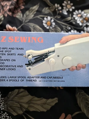E-Z Sewing – Smidig handhållen symaskin i originalkartong - Säljer en praktisk handhållen symaskin som är idealisk för dig som snabbt vill kunna fixa fållar eller laga revor utan att behöva ta fram den stora symaskinen. Den är så kompakt att du kan fålla gardiner direkt på stången eller laga byxor "på språng". Skick: Knappt använd och i mycket gott skick (se bilder). Portabel: Drivs av 4 st AA-batterier (ingår ej), vilket gör den helt sladdlös. Komplett: Säljes i originalförpackning med tillbehör (trådrullar, nålpåträdare, extra nål och adapter för spola