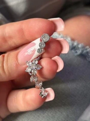 Silvrigt navelpiercingsmycke med blommor - Säljer ett silvrigt navelpiercingsmycke med gnistrande stenar i blommönster. Smycket har tre runda stenar upptill och flera små blommor som hänger nedåt. Perfekt för dig som vill ha något glittrigt och unikt till din piercing.