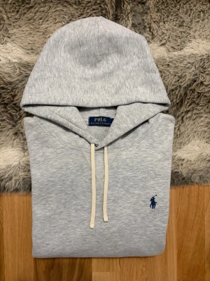 Ljusgrå Polo Ralph Lauren Fleece Hoodie - Storlek XL - Hej! 👋 Säljer en riktigt snygg ljusgrå Polo Ralph Lauren fleece hoodie i storlek XL med marinblå pony. 🐎 Tröjan är i mycket gott skick och känns fräsch. Det finns en liten fläck högst upp på höger ärm vid axeln (se bild), inget som stör vid användning. ✨ 100% äkta med tvättlappar och fungerande QR-kod för enkel verifiering ✅ En klockren och bekväm klassiker i en rymlig storlek! Fraktar snabbt! 🚛📦💬 