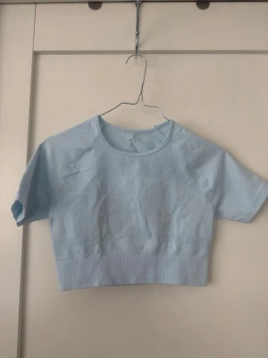 Ljusblå cropped topp med cut-out - Trendig ljusblå cropped topp med korta ärmar och rund halsringning. Toppen har en snygg cut-out detalj i ryggen och bred ribbad kant nedtill. Perfekt för en sportig och avslappnad stil.
