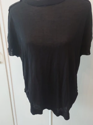 Svart loose top med kort ärm - En svart top med loose passform och korta ärmar. Toppen har rund halsringning och är tillverkad i ett tunt, lätt material som ger en avslappnad look. 