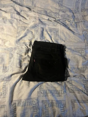 Svarta jeans från Levi's - Snygga svarta jeans från Levi's 511 med klassisk femficksdesign och rakt ben. Jeansen har Levi's ikoniska röda etikett på bakfickan och är tillverkade i ett mjukt denimtyg som sitter skönt. Perfekta för en stilren och avslappnad look. W30 L30 slim fit.