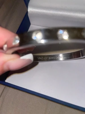 Silverfärgat armband SNÖ of Sweden - Snyggt och stilrent armband i silverfärgad metall från SNÖ of Sweden. Armbandet har en rundad form och är dekorerat med gnistrande stenar längs hela bandet för en extra lyxig känsla.