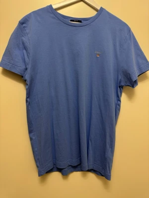 Blå t-shirt från Gant - Snygg blå t-shirt från Gant med liten broderad logga på bröstet. Klassisk rund halsringning och korta ärmar. Tillverkad i mjuk bomull som känns skön mot huden. Perfekt för en avslappnad och stilren look.