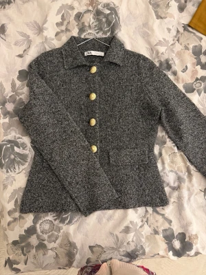 Grå tröja från ZARA med guldknappar - Stilren grå ”kavajtröja” från ZARA✨ Tröjan har klassisk krage, figurnära passform och två fickor framtill. Materialet är mjukt och har en lätt melerad struktur som ger en modern look✨✨
