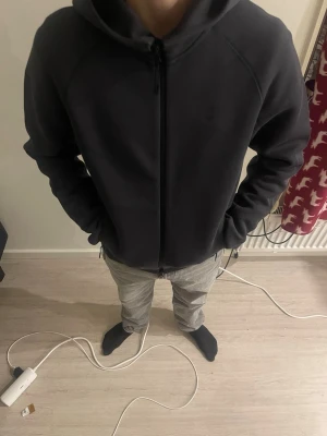 Mörkgrå Nike hoodie med dragkedja - Säljer en mörkgrå hoodie från Nike med hel dragkedja framtill och två fickor med dragkedja. Hoodien har en stilren design med diskret Nike-logga på bröstet och huva. Perfekt för dig som gillar sportig och avslappnad stil.