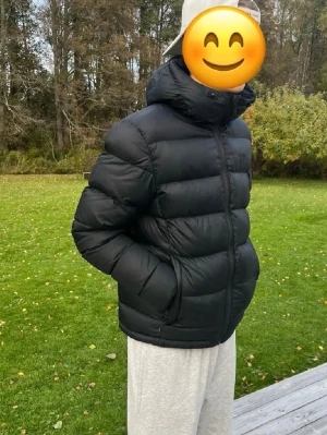Svart pufferjacka med huva - Säljer en svart pufferjacka med huva och dragkedja framtill. Jackan har en klassisk quiltad design med breda kanaler och två sidofickor. Perfekt för kalla dagar och riktigt skön att bära. Passar dig som gillar en stilren och enkel look.