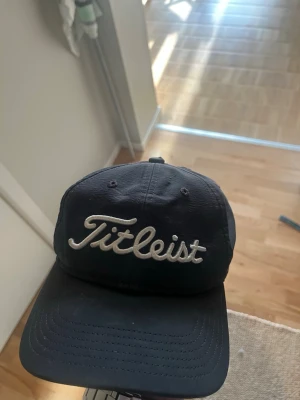 Svart Titleist golfkeps - Snygg svart keps från Titleist med broderad logga framtill och texten 'Pro V1' på sidan. Klassisk böjd skärm och justerbar passform. Perfekt för golfbanan eller som sportig accessoar. Tillverkad i slitstarkt tyg.