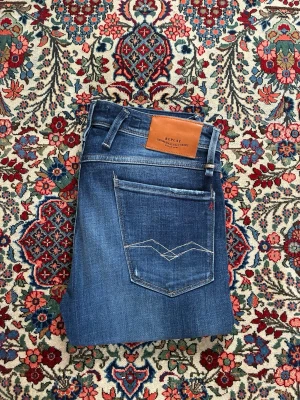 Replay jeans - Säljer ett par klassiska blå jeans från Replay med snyggt slitna detaljer och kontrastsömmar. De är knappt använda och ser samt känns nya. Vid frågor eller funderingar tveka inte på att höra av er! 