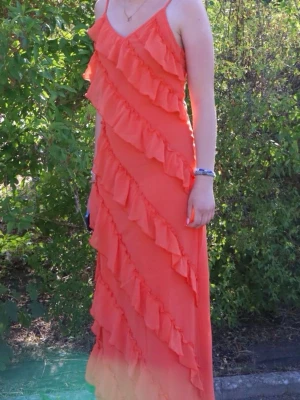 Orange långklänning med volanger - Säljer en snygg orange långklänning med tunna axelband och diagonala volangdetaljer över hela klänningen. Klänningen har en v-ringad hals och är perfekt för sommarens alla tillfällen. Materialet känns lätt och luftigt.🤗🤗