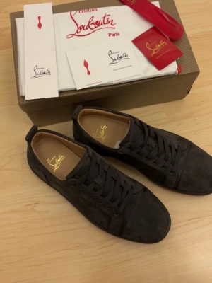  Christian Louboutin - Stilrena gråa sneakers från Christian Louboutin i mocka med matchande gråa skosnören och diskret logga på innersulan. Klassisk låg modell med rund tå och svart yttersula. Perfekta för dig som gillar exklusiva och tidlösa skor.
