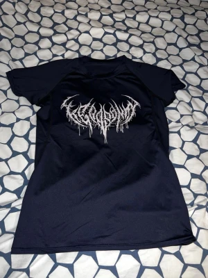 Svart t-shirt med tryck - Snygg svart t-shirt med ett vitt, metallinspirerat tryck på bröstet. T-shirten har korta ärmar och är gjord i ett mjukt syntetmaterial som känns skönt mot huden. Perfekt för dig som gillar alternativ stil och vill sticka ut.