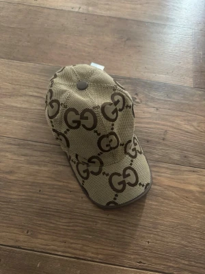 Beige G keps  - Säljer en beige keps  med  brunt över hela kepsen. Kepsen har böjd skärm och justerbar rem bak. Materialet är canvas med bruna detaljer och insidan är fodrad i brunt tyg. Perfekt för dig som gillar exklusiva accessoarer.