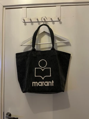 Shoppingväska från Isabell Marant  - Stilren shoppingväska från Isabell Marant.  Väskan har två rejäla handtag och ett vitt tryck med Marant-logga på framsidan. Perfekt storlek för att bära med sig allt man behöver. Enkel och trendig design.