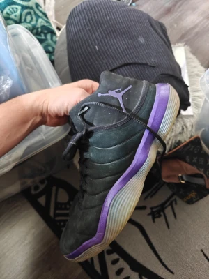 Svarta Air Jordan sneakers med lila sula Helg REA NU! - Säljer ett par svarta Air Jordan sneakers med lila detaljer och genomskinlig sula. Skorna har klassisk Jordan-logga på sidan och tungan, samt svarta skosnören. Ovandelen är i mocka och designen är sportig och clean. BJ1 Helg Rea