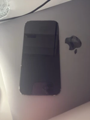 Svart iPhone  12 med dubbla kameror - Säljer en svart iPhone med stilren design och dubbla kameror på baksidan. Telefonen har en platt framsida med stor skärm och rundade hörn. Tillverkad i glas och metall, klassisk Apple-logga på baksidan. Perfekt för dig som gillar snygg och modern teknik.