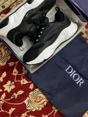 Svarta Dior sneakers med vit sula - Snygga svarta Dior sneakers med chunky vit sula. Skorna har en mix av mesh och läderdetaljer, svarta skosnören och diskret Dior-logga på sidan. Modern och sportig design som sticker ut.