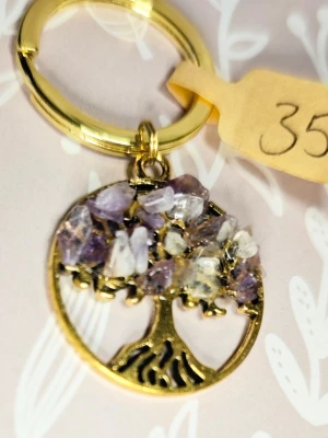 Nyckelring med livets träd och ametist kristaller - Snygg nyckelring i guldfärgad metall med ett trädformat hänge dekorerat med små lila och genomskinliga kristaller. Perfekt accessoar för att piffa upp väskan eller nyckelknippan. Trädet har fina detaljer och ger en magisk känsla.