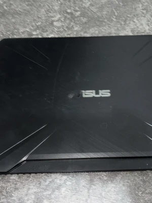 Svart ASUS TUF Gaming laptop - Säljer en svart ASUS TUF Gaming bärbar dator med stilren design och markerade linjer på locket. Tangentbordet har vita WASD-tangenter och datorn har AMD Ryzen-märke. Perfekt för gaming och studier, med robust plastchassi och stor skärm.