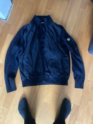 Mörkblå cardigan från J.Lindeberg - Pris kan diskuteras! Snygg mörkblå cardigan från J.Lindeberg med ribbade muddar och krage. Passar M och S. Jackan har en klassisk zip framtill och en patch med logga på ärmen. Materialet är en mix av glansig nylon och stickad bomull vilket ger en modern look. 