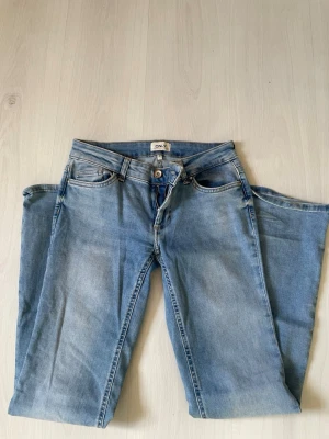 Ljusblå jeans från ONLY - Säljer ett par ljusblå jeans från ONLY med klassisk femficksmodell och dragkedjegylf. Jeansen har raka ben och är tillverkade i mjukt denimtyg som ger en avslappnad look. Perfekta till sneakers eller boots för en trendig vardagsstil.