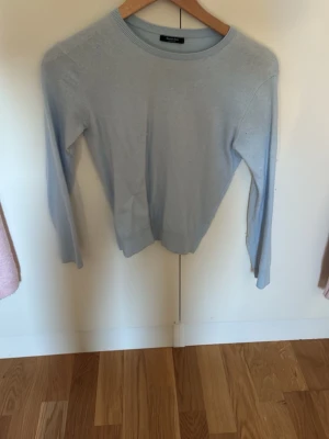 Ljusblå enkel tröja med rund hals - En stilren ljusblå tröja med rund halsringning och långa ärmar. Tröjan har en smal passform och ribbade muddar vid ärmslut och nederkant. Perfekt att matcha med jeans eller kjol för en clean look.