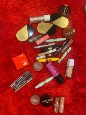 Stort sminkpaket från IsaDora & Maybelline - Säljer ett stort sminkpaket med flera produkter från IsaDora och Maybelline. Innehåller puder, foundation, concealer, mascara, läppstift, läppglans och ögonpennor i olika färger som nude, rosa, brun och guld. Perfekt för dig som vill testa olika basprodukter och sminklooker.