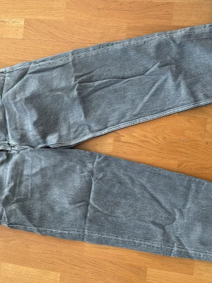 Grå raka jeans i klassisk modell - Säljer ett par grå jeans med rak passform och hög midja. Jeansen har en klassisk femficksdesign och är tillverkade i ett mjukt denimtyg. Perfekta för en avslappnad och stilren look.