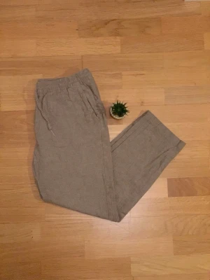 Beige linnebyxor med dragsko - Säljer ett par beige linnebyxor med avslappnad passform och resår i midjan samt dragsko. Byxorna har raka ben och sidofickor, perfekta för en chill och stilren look. Materialet är luftigt linne som passar bra till varmare dagar.