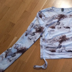 Långärmad tie-dye topp med snörning - Trendig långärmad topp med brun och vit tie-dye effekt. Toppen har snörning i sidan för en justerbar passform och croppad look. Tillverkad i mjukt material som känns skönt mot huden. Perfekt för dig som vill ha en unik och stilren vibe.
