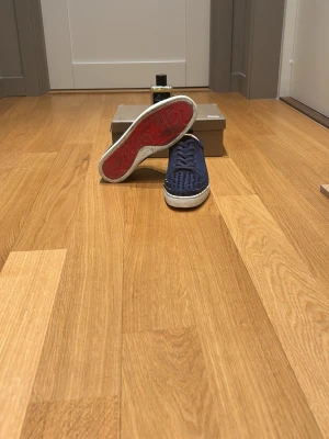 Marinblå Christian Louboutin sneakers+ parfym på köpet! - Snygga marinblå sneakers från Christian Louboutin med klassiska röda sulor och coola nitar på tån. Skorna har en låg profil och är gjorda i mocka med vita gummisulor. Perfekta för dig som vill sticka ut med en exklusiv och edgy stil. Och en väldigt bra dupe på layton!