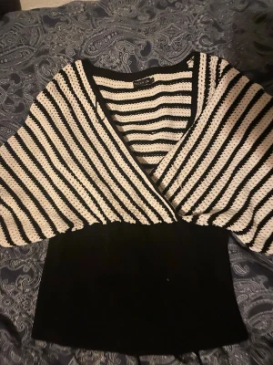 Randig stickad topp från Boohoo - Säljer en svartvit stickad topp från Boohoo med breda, fladdriga ärmar och djup v-ringning. Överdelen har ett coolt randigt mönster i svart och vitt, medan nederdelen är helsvart och ribbstickad. Perfekt för dig som gillar unik och trendig stil.