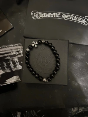 😎 pärlarmband Chrome Hearts svart grisch - Snyggt svart pärlarmband från Chrome Hearts med silverdetaljer och ikonisk korsberlock. Armbandet består av svarta runda pärlor och flera små silvriga detaljer som ger en cool kontrast. Perfekt accessoar för dig som gillar exklusiv och edgy stil.