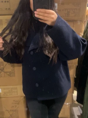 Blå kappa (LÅNAD BILD FRÅN HEMSIDAN)  - Blå kappa med unik asymmetrisk knäppning framtill. Jackan har en hög krage, stora knappar och en loose passform. 