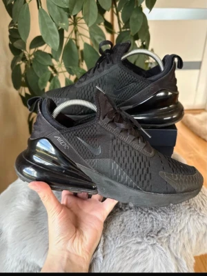 Nike Air Max 270 helsvarta sneakers - Snygga helsvarta Nike Air Max 270 sneakers med mesh-ovandel och stora luftbubblor i hälen. Skorna har diskreta loggor på sidan och tungan, samt svarta snören och detaljer. Perfekta för dig som gillar sportig och modern stil. Nyrengorda men börjar ta slut på luft i sulan, inte än men börjar!