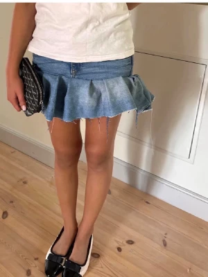 Blå jeanskjol med volangkant - Trendig kort jeanskjol i blå denim med volangkant. Storlek XS
