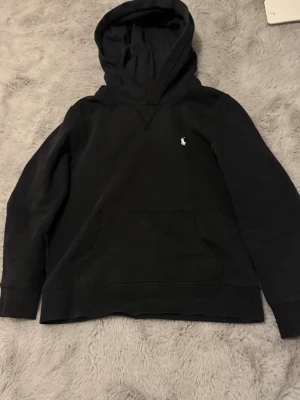 Ralph lauren hoodie xxs - Säljer svart Ralph lauren hoodie i Stl 10-12y vilket motsvarar ca 152 men använd upp till ca 165 så passar större. Den har ett hål på armbågen men det syns knappt när man har armen rak. Den är inte tväddad så därav lite fläckar mm på bild men tvättas såklart innan jag postar. Hör av er vid frågor