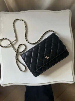 svart quiltad handväska - Säljer en klassisk svart quiltad handväska med guldfärgad kedjerem och ikonisk CClogga framtill. Väskan är tillverkad i läder med elegant struktur och har en tidlös design som passar till många olika looks.