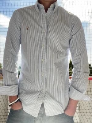 Randig skjorta från Polo Ralph Lauren - Snygg vit och blå randig skjorta från Polo Ralph Lauren i slim fit-modell. Skjortan är perfekt för sommaren. Priset går att diskutera skicka gärna bud 
