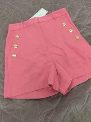 Rosa shorts med guldknappar - Rosa shorts med hög midja och guldknappar. 
