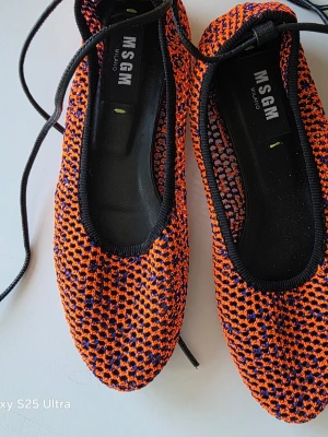 MSGM stickade ballerinaskor orange/svart - Snygga ballerinaskor från MSGM i stickat material med orange och svarta detaljer. Skorna har svarta kanter och långa snören att knyta runt ankeln. Mjuka och flexibla med rund tå och låg sula. Perfekta för dig som gillar färg och mönster.