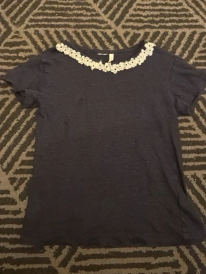 Mörkblå t-shirt med spetsdetalj - Snygg mörkblå t-shirt med korta ärmar och vit spets längs halsringningen. Perfekt för dig som gillar enkla plagg med en twist. Tillverkad i mjuk bomull, så väldigt skön mot huden, tyvärr är lappen avklippt så jag ser inte storleken men jag skulle uppskatta att den är mellan xs och s förutom det är den i väldigt bra skick. Tveka inte på att höra av dig för fler frågor eller bilder🤗