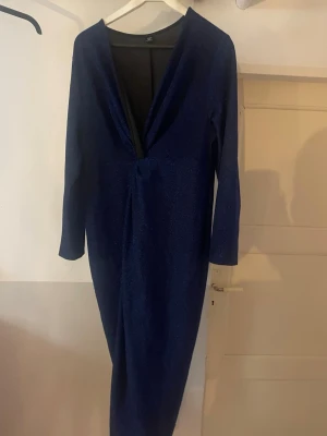 Marinblå glittrig långklänning Shein - Snygg marinblå långklänning från Shein med glittrigt tyg och djup v-ringning. Klänningen har långa ärmar och en elegant, figurnära passform som passar perfekt till speciella tillfällen.
